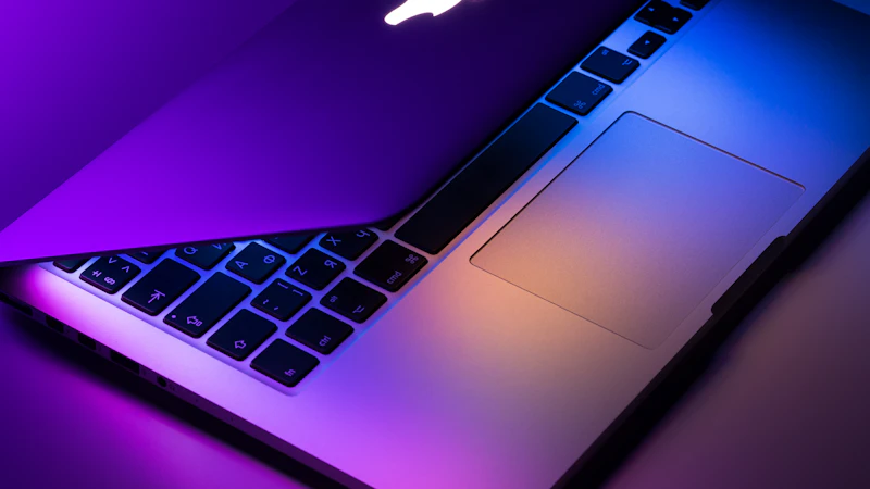 Close-up of a MacBook keyboard and trackpad lit in purple and blue